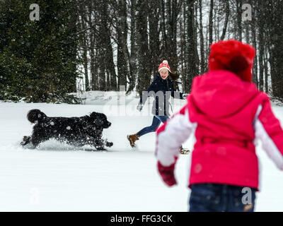 Due sorelle a giocare nella neve con il cane newfoundlander, inverno e tempo libero Foto Stock