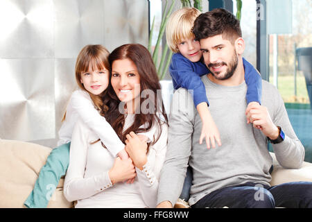 Ritratto di felice giovane famiglia con due bambini seduti al divano e smilig. Padre Felice dando sovrapponibile a suo figlio carino. Foto Stock