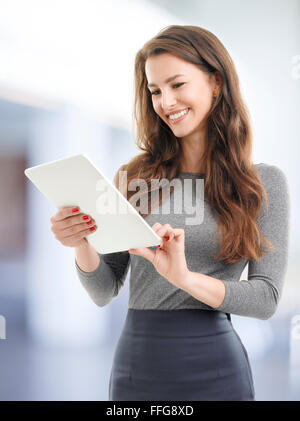 Immagine della bella giovane donna in piedi tenendo tavoletta digitale nelle sue mani e la lettura del testo. Imprenditrice lavorando Foto Stock