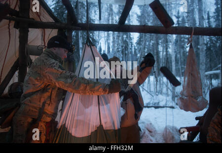 Il personale Sgt. Seth Reab, det. 1, 66Training Squadron, detiene un paracadute come Capt. Bart Spendley, 274th aria funzionamento supporto Squadron, aria liaison officer, si svuota la neve per acqua durante arctic survival training. Foto Stock