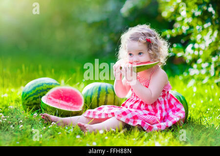 Bambino mangiare anguria in giardino. I bambini mangiano la frutta all'esterno. Snack sani per i bambini. Bambina Giochi nel giardino Foto Stock