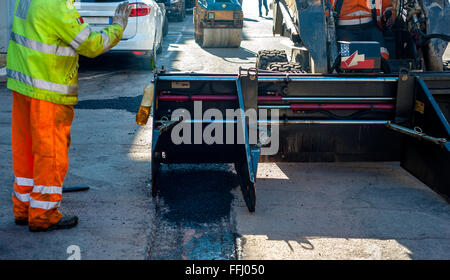 Lavoratore di asfalto operativo lastricatore macchina durante la costruzione di strade e lavori di riparazione Foto Stock