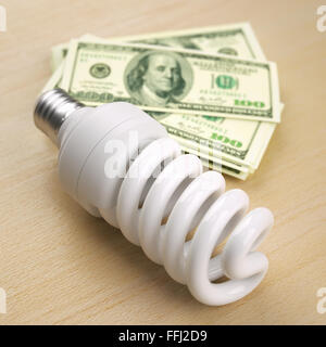 Lampada compatta a fluorescenza di fronte a un centinaio di dollari pila Foto Stock