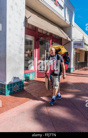 Un vecchio maschio transitoria zaino in spalla porta il suo mondo possedimenti sulla sua schiena come egli cammina su State Street a Santa Barbara, CA. Foto Stock