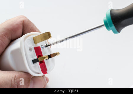 Maschio bianco mano utilizzando un cacciavite fissa una vite in un nazionale di spina elettrica. Sfondo bianco con copia area spazio per hom Foto Stock