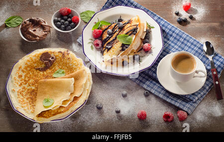 Frittelle con frutti di bosco freschi, crema di cioccolato e la tazza di caffè per colazione. Vista superiore Foto Stock