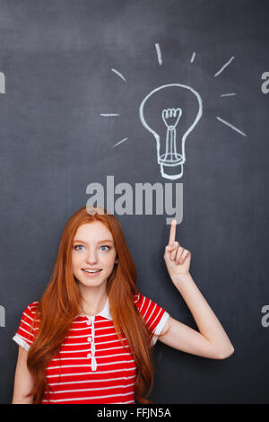 Ispirato attraente giovane donna con i capelli rossi rivolta verso l'alto ed avente un'idea su sfondo blackboard Foto Stock