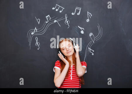 Rilassato sorridente bella giovane donna ascoltando la musica nelle cuffie su sfondo lavagna Foto Stock