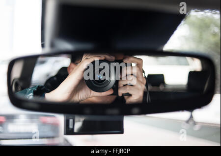 Uomo in possesso di una fotocamera si siede sul sedile conducente e guarda nello specchietto retrovisore Foto Stock