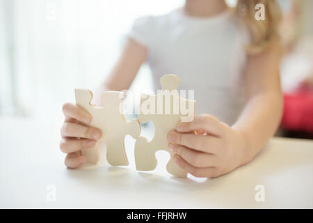 Bambino ragazza con due grandi puzzle in legno pezzi. Mani il collegamento di puzzle. Close up foto con piccole dof. L educazione e l apprendimento del concetto. Foto Stock