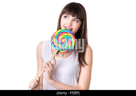 Headshot Ritratto di giovane bella donna giocoso azienda enorme colorati di forma rotonda lecca-lecca, studio, sfondo bianco Foto Stock