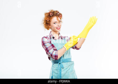 Felice giovane e bella casalinga in grembiule blu indossando guanti di colore giallo su sfondo bianco Foto Stock