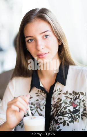 Giovane bella donna con lei ogni mattina il latte nel ristorante. Splendida ragazza studente agitazione prima colazione caffè nella caffetteria Foto Stock