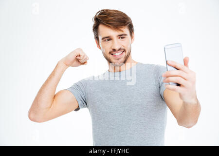 Uomo felice rendendo selfie foto sullo smartphone e mostrando il suo bicipite isolato su uno sfondo bianco Foto Stock