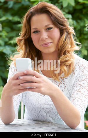 Ragazza adolescente nel giardino di inviare un messaggio di testo Foto Stock