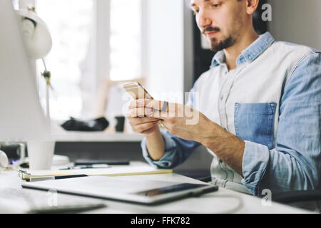 Imprenditore bello lavorare in ufficio utilizzando il telefono cellulare Foto Stock