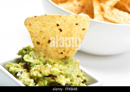 Primo piano di una vaschetta quadrata con il guacamole e una ciotola rotonda con nachos in background Foto Stock
