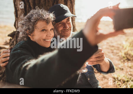 Felice coppia senior tenendo la loro auto ritratto con il loro telefono cellulare sul campeggio giorno. L uomo e la donna seduta insieme all'aperto presso Foto Stock