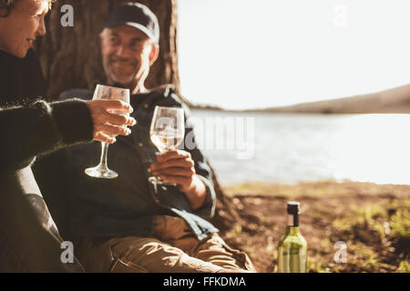 Close up ritratto della coppia senior bere il vino durante il campeggio vicino a un lago. Concentrarsi sulle mani tenendo un bicchiere di vino. Foto Stock