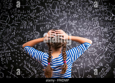 Pensare ragazza tenendo la testa contro la grande lavagna, vista posteriore Foto Stock