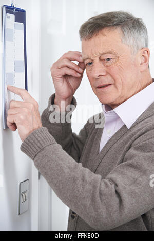 Confuso uomo anziano con demenza guardando il calendario da parete Foto Stock