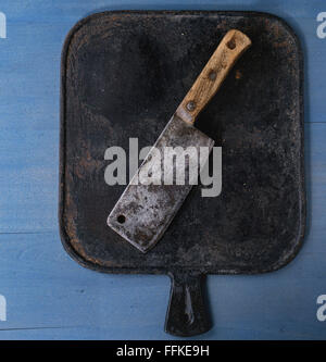 Vecchia macelleria vintage cleaver su nero tagliere blu su una superficie di legno. Vista dall'alto. Foto Stock