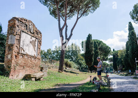 Un maschio di turista con la sua bicicletta una sosta per ammirare un monumento storico sulla Via Appia / Via Appia Antica di Roma, Italia. Foto Stock