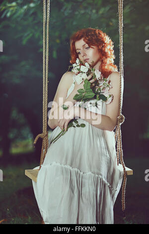 Romantico ritratto di una bella donna con i capelli rossi. Swing in una foresta Foto Stock