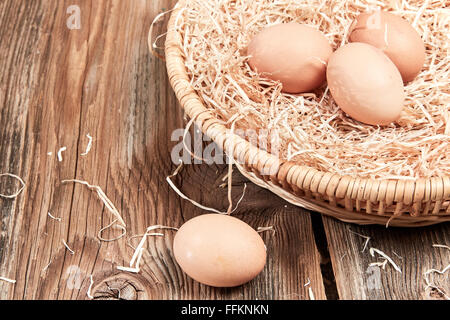 Tre uova fresche in un cesto di pasqua e un uovo sul tavolo di legno. Foto Stock