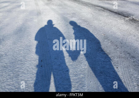 Ombra di un paio di piedi insieme su una giornata invernale e. Essi ombra di un uomo e di una donna tenendo le mani è gettato nella terra. Foto Stock