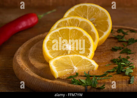 Fette di limone e peperoncino rosso sul tagliere di legno con prezzemolo Foto Stock