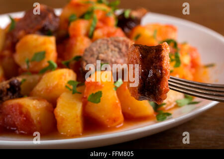 Sulla fetta di salsiccia nella forcella con spezzatino di patate in background Foto Stock