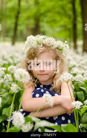 Adorabile bionda ragazza seduta tra i fiori bianchi nel verde dei boschi Foto Stock