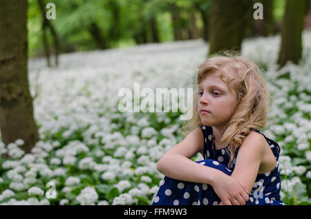 Adorabile bionda ragazza seduta tra white flowersf nel verde dei boschi Foto Stock