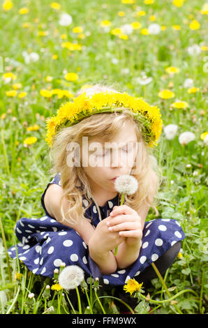 Bella ragazza bionda seduta nel prato con tarassaco catena sopra la testa Foto Stock