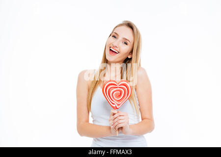 Felice eccitato giovane donna in piedi e tenendo a forma di cuore ad lollipop su sfondo bianco Foto Stock