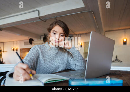 Donna che lavorano con il computer portatile e il blocco note in cafe Foto Stock