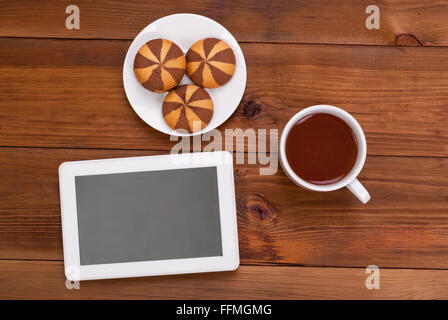 Tazza di tè e biscotti una tavoletta digitale sul tavolo di legno. Vista superiore . Foto Stock