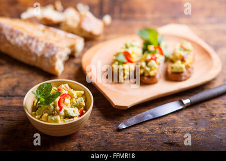 Avocado spalmato su fette di bruschetta contro il tavolo di legno Foto Stock