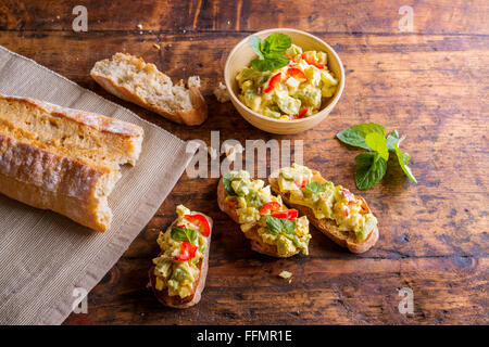 Avocado spalmato su fette di bruschetta contro il tavolo di legno Foto Stock