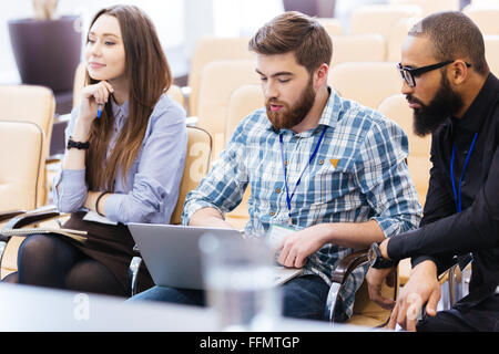 Gruppo multietnico di giovani uomini di affari con computer portatile seduti sulla riunione in sala conferenze Foto Stock