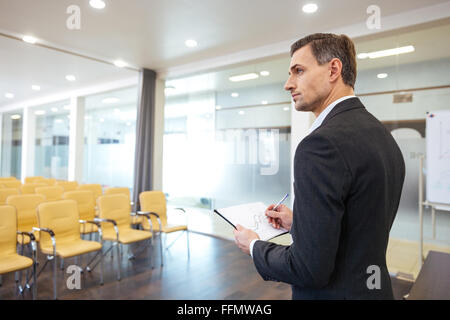 Malinconici bello imprenditore con appunti in piedi in conferenza vuota hall Foto Stock