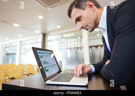 Profilo di focalizzata serio uomo al lavoro con il computer portatile nella vuota sala conferenza Foto Stock