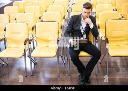Imprenditore concentrato lavora con la compressa nella vuota sala conferenza Foto Stock