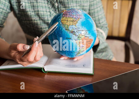 Mano femmina con penna e un globo del puzzle Foto Stock