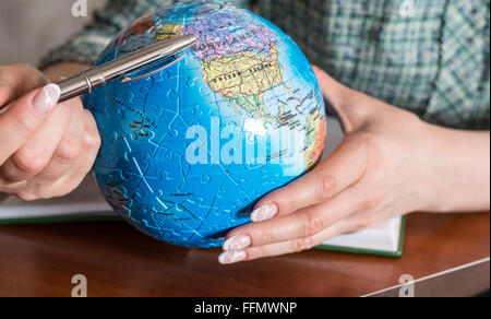 Mano femmina con penna e un globo del puzzle Foto Stock