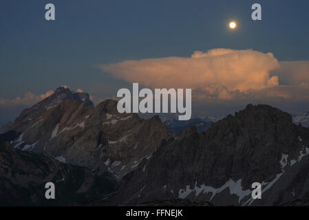 Full Moon Rising durante l'incandescente tramonto sul Monte Drusenfluh e Kirchlispitzen visto da Totalp baita di montagna, Austria Foto Stock