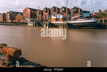 Fiume scafo ad alta marea con un obsoleto peschereccio nel fango bank affiancato da ufficio e di altri edifici di Hull, Yorkshire Foto Stock