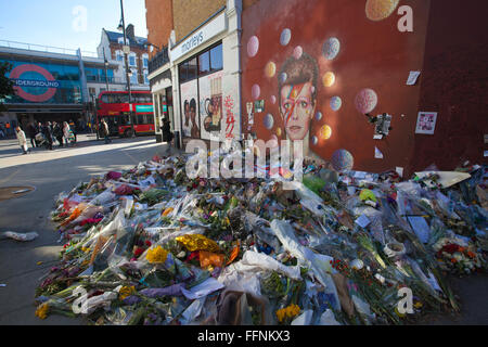 Fiori a sinistra sotto un David Bowie 'Aladdin Sane' murale su una parete di strada in Brixton, realizzato in un santuario di fortuna dopo la sua morte. Foto Stock