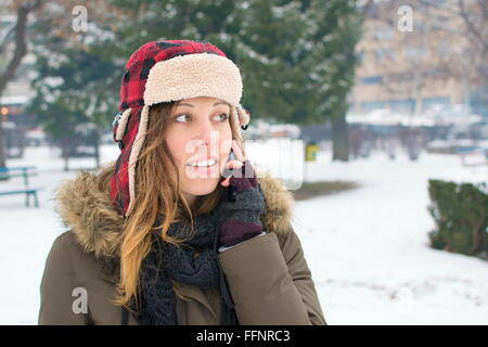 Ragazza con un taglialegna hat parlando sul suo cellulare nella neve Foto Stock